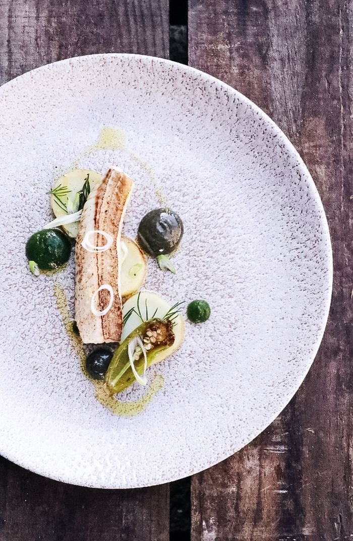 Top view of delicious fish slice with sauce and onion slices with herbs and green pepper on white plate placed on wooden surface in light restaurant